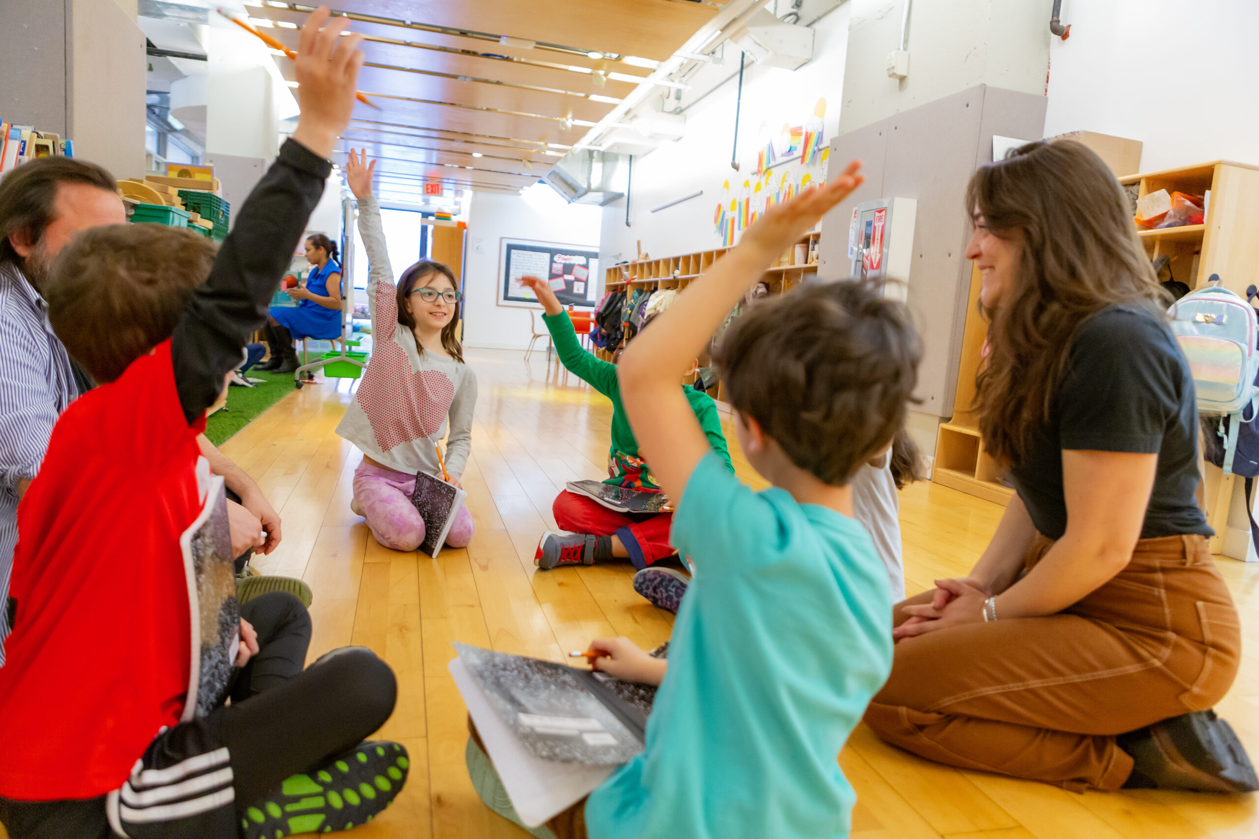 Group of students raising hand sitting in a circle with teachers.